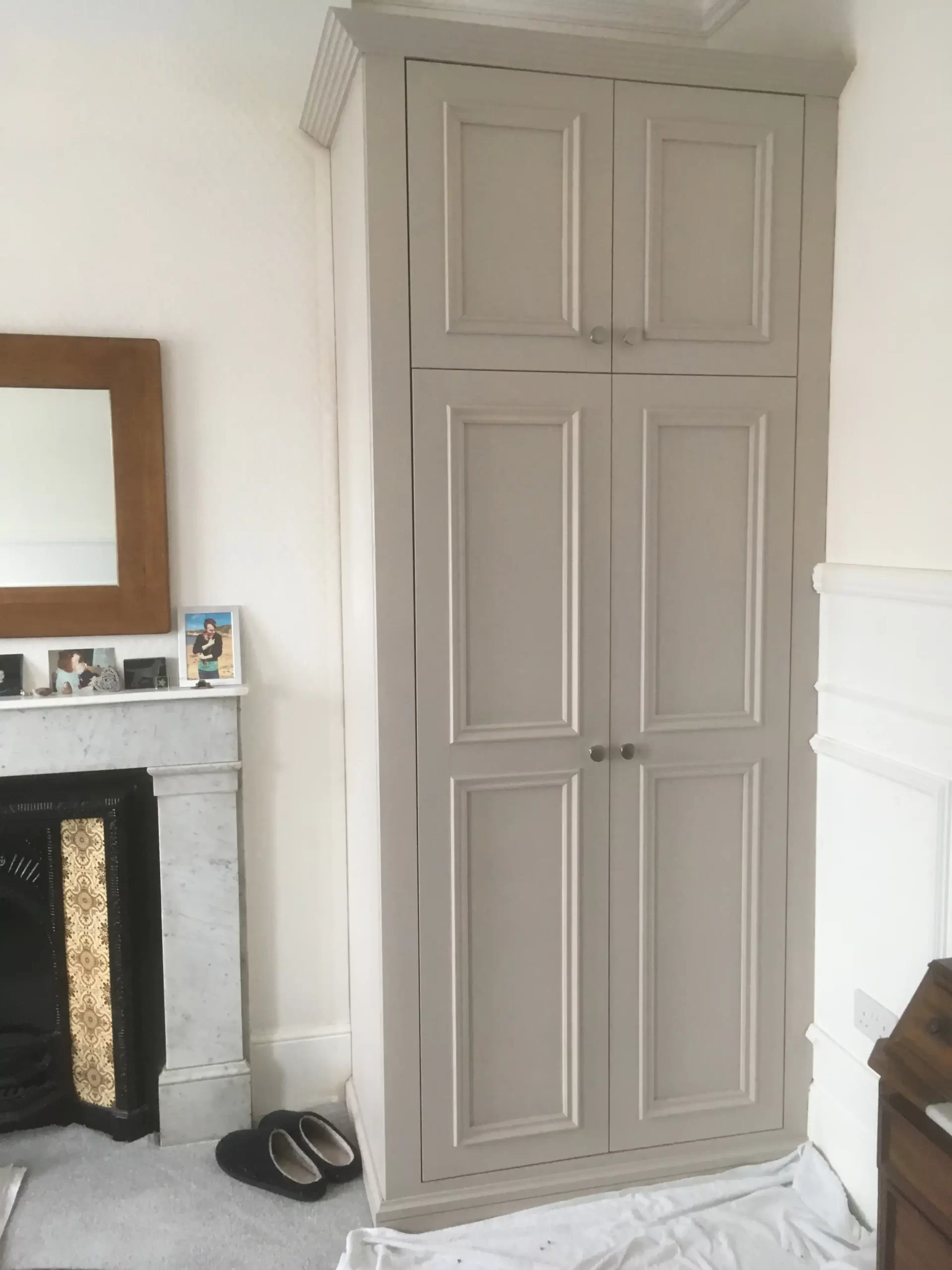 Bespoke alcove fitted wardrobe with detailed panelling and top storage doors.